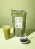 A glass of green liquid, a bag of green powder, and a small bowl of green powder with a utensil are arranged on a light green surface against a light green background. Produktbild-Vorschau