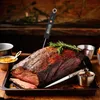 A roasted piece of meat with a thermometer inserted, garnished with rosemary, and served with side dishes. Produktbild-Vorschau