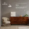 A retro-style mini-refrigerator is displayed on a wooden dresser in a room with a chair and a floor lamp. Produktbild-Vorschau