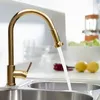 A gold kitchen faucet with water running into a sink, with lemons and a bowl of salad in the background. Podgląd zdjęcia produktu