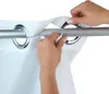 Hands adjusting a white fabric shower curtain with grommets onto a silver shower curtain rod. Produktbild-Vorschau
