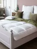 A cozy bedroom scene with a bed made up with a white duvet and pillows, and a green throw blanket. Produktbild-Vorschau