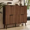 A wooden cabinet with fluted doors and dark handles, placed in a room with a plant and a window view. Anteprima dell’immagine prodotto