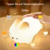 A hand is touching a glowing bunny-shaped night light, with various color options and modes indicated by text and icons around it. Produktbild-Vorschau
