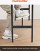 A person's legs and feet are shown resting on the footrest bar of a bar table. Produktbild-Vorschau