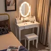 A white vanity table with a lighted mirror and stool, set up in a bedroom next to a bed. Voir les images du produit