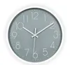 A minimalist wall clock with a gray face and white numbers and hands, set against a white background. Náhled obrázku produktu