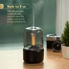 Aroma diffuser with a candle-like light, emitting mist, placed on a wooden surface with a vintage camera and a small plant in the background. Podgląd zdjęcia produktu