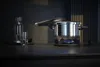 A pressure cooker is on a stove with a blue flame, next to a glass bottle and a glass of water. Náhled obrázku produktu