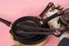 A set of frying pans and kitchen tongs are arranged on a wooden board against a pink background. Náhľad obrázku produktu