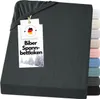 A dark gray fitted sheet is displayed, with a tag attached to the top corner. A stack of differently colored fitted sheets is visible on the right side of the image.