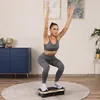 A woman is performing a squat exercise on a vibrating platform in a room. Náhľad obrázku produktu