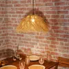 A hanging lamp made of straw-like material is illuminated above a wooden table set with plates and glasses. Produktbild-Vorschau