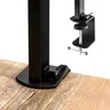A close-up view of a black desk lamp's base and clamp mechanism attached to a wooden surface. Náhled obrázku produktu