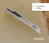 A metal engraving tool with a textured handle rests on a light brown surface, with a wooden texture visible on the right side. A white box with text and a checkmark is in the upper right corner, and a brand logo is in the lower right corner. Produktbild-Vorschau