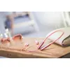 A pair of rose pink in-ear headphones are laid out on a wooden surface next to a clutch purse and sunglasses. Produktbild-Vorschau