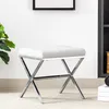 A white upholstered stool with a chrome X-shaped base is shown in a room with a plant and a bookshelf in the background. Produktbild-Vorschau