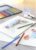 A watercolor painting setup with colored pencils, a glass of water, and a brush on a wooden table. Podgląd zdjęcia produktu