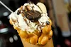 Close-up of a sweet bubble waffle cone filled with whipped cream, chocolate drizzle, Oreos, and other toppings. Náhľad obrázku produktu