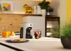 A kitchen counter scene with a coffee machine, juice, oranges, and cookies. Produktbild-Vorschau