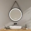 A round LED mirror with a black frame hangs above a white vessel sink on a wooden vanity. The mirror has a bright LED light around its edge and touch controls in the center. There are two black wall-mounted fixtures above the sink, and a soap dispenser and Anteprima dell’immagine prodotto