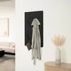 A modern entryway or hallway with a black coat rack mounted on a white wall, holding a light gray coat and a brown clutch bag. A vase with dried pampas grass sits on a wooden cabinet to the right. Náhled obrázku produktu