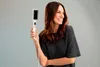 A woman is holding a hair straightening brush and smiling. Produktbild-Vorschau
