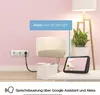 A smart plug is shown connected to a wall socket, with a digital assistant device on a table in the foreground. The scene is set in a room with pink walls and a floor lamp. Voir les images du produit