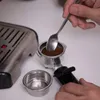 A person is using a spoon to add coffee grounds to an espresso machine portafilter. Produktbild-Vorschau