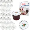 A collection of small glass jars with decorative lids, a jar filled with jam, a recipe book, and a decorative plate, all with a Christmas theme. Voir les images du produit