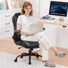 A woman is sitting in a gaming chair at a desk with a laptop and computer. Produktbild-Vorschau