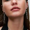 Close-up of a woman's face and neck, wearing silver chain link earrings and a silver chain necklace. Anteprima dell’immagine prodotto