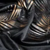 A close-up shot of black fabric with a metallic palm leaf pattern in gold and silver. Produktbild-Vorschau