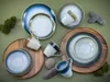 A collection of stoneware plates and mugs arranged on a green surface, with natural elements like moss and stones. Náhľad obrázku produktu
