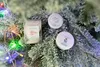 Several small holiday-themed gift items are nestled amongst the branches of a frosted Christmas tree, adorned with colorful lights. Produktbild-Vorschau