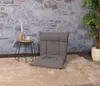 A floor chair is placed on a fluffy rug in front of a stone wall, with a small side table and a plant nearby. Produktbild-Vorschau