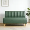 A green sofa in a room with a white wall and a framed picture. Produktbild-Vorschau