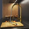 A modern kitchen sink area with a gold faucet and a pull-out spray head over a wooden cutting board with oranges. Podgląd zdjęcia produktu