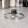 A glass pot lid with a black handle sits on a speckled gray countertop. Náhled obrázku produktu