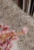 A close-up of a textured rug with a vase of pink flowers in the foreground. Voir les images du produit