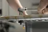 A person is using a socket wrench to tighten a bolt on a metal fixture, likely part of a kitchen sink installation. Produktbild-Vorschau
