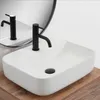A white rectangular basin sink with a black faucet is shown on a wooden countertop, with a mirror reflecting the sink and faucet. Náhľad obrázku produktu