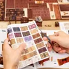 A person is cutting out stickers of miniature books from a sheet, with a partially assembled 3D book nook kit in the background. Voir les images du produit