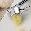 A close-up of a metal garlic press with crushed garlic being squeezed out. Náhled obrázku produktu