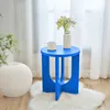A blue side table with a mug and a vase of flowers on it, placed on a white rug in a room with sheer curtains. Produktbild-Vorschau