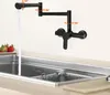 A black kitchen faucet mounted on a wall above a sink, with water running into the sink. Strawberries are visible on a plate to the left. Podgląd zdjęcia produktu