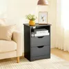 A black nightstand is placed next to a beige sofa in a room. Náhled obrázku produktu