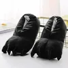 A pair of black, plush slippers shaped like monster or animal paws with claws, placed on a white surface with a blurred background. Náhled obrázku produktu