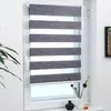 A close-up view of a roller blind in a window, with a plant on the left and decorative items on the windowsill. Produktbild-Vorschau