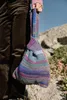 A person holding a colorful knitted bag outdoors with rocks and plants in the background. Produktbild-Vorschau